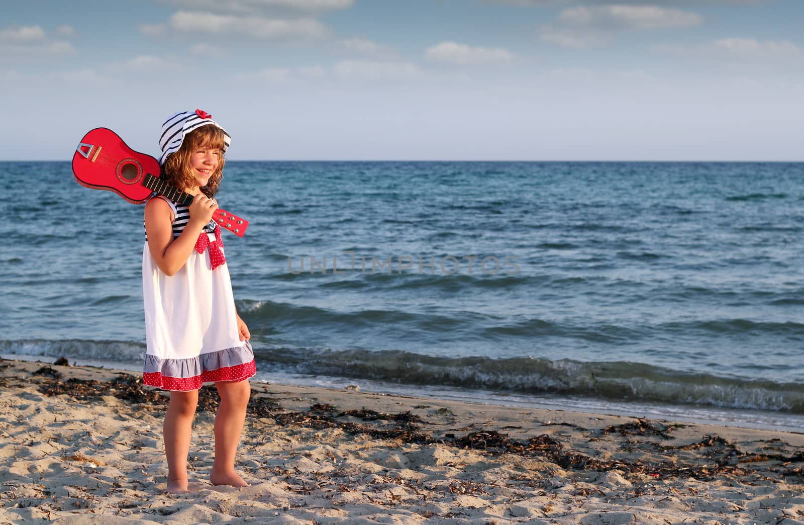 happy little girl with guitar on beach by goce