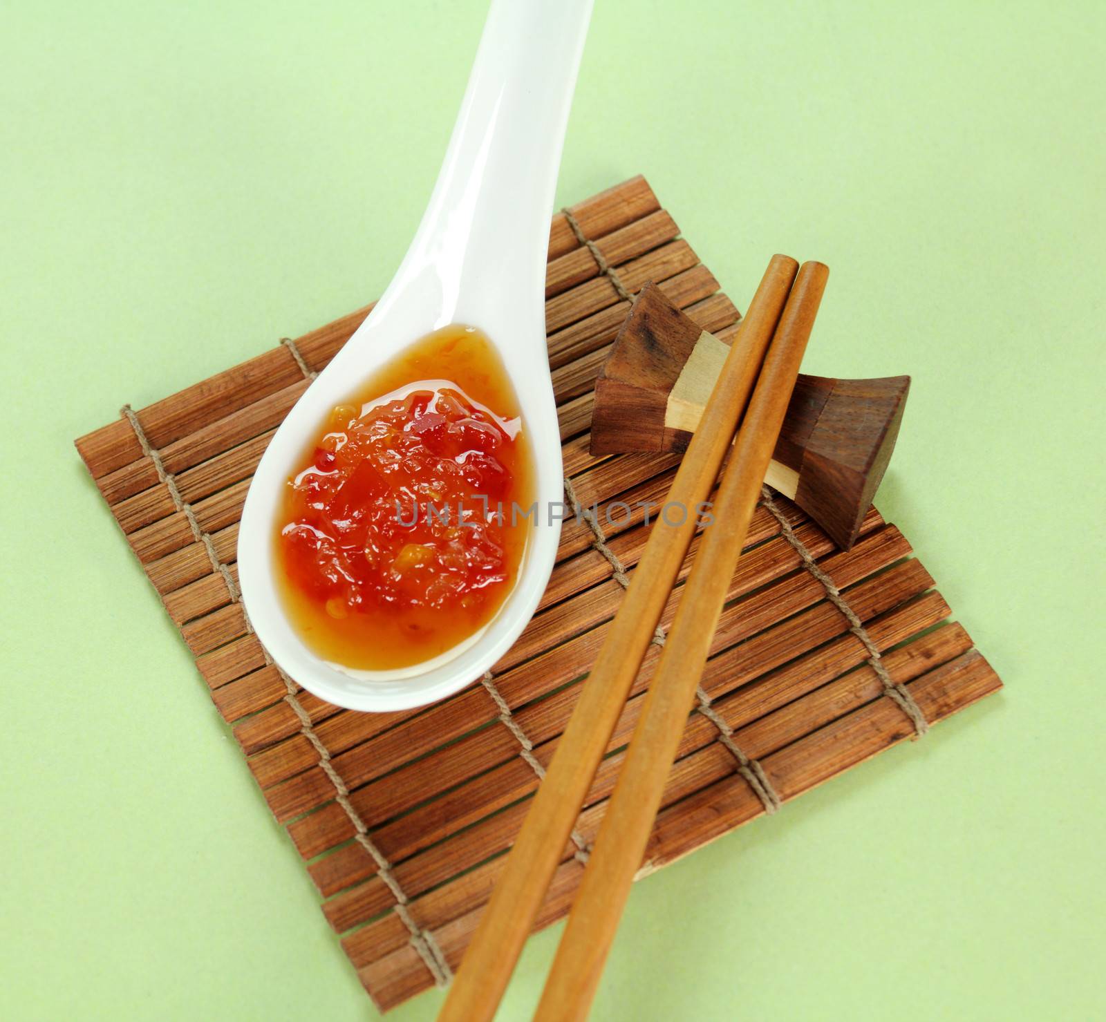 Sweet chilli sauce in a spoon with chopsticks.