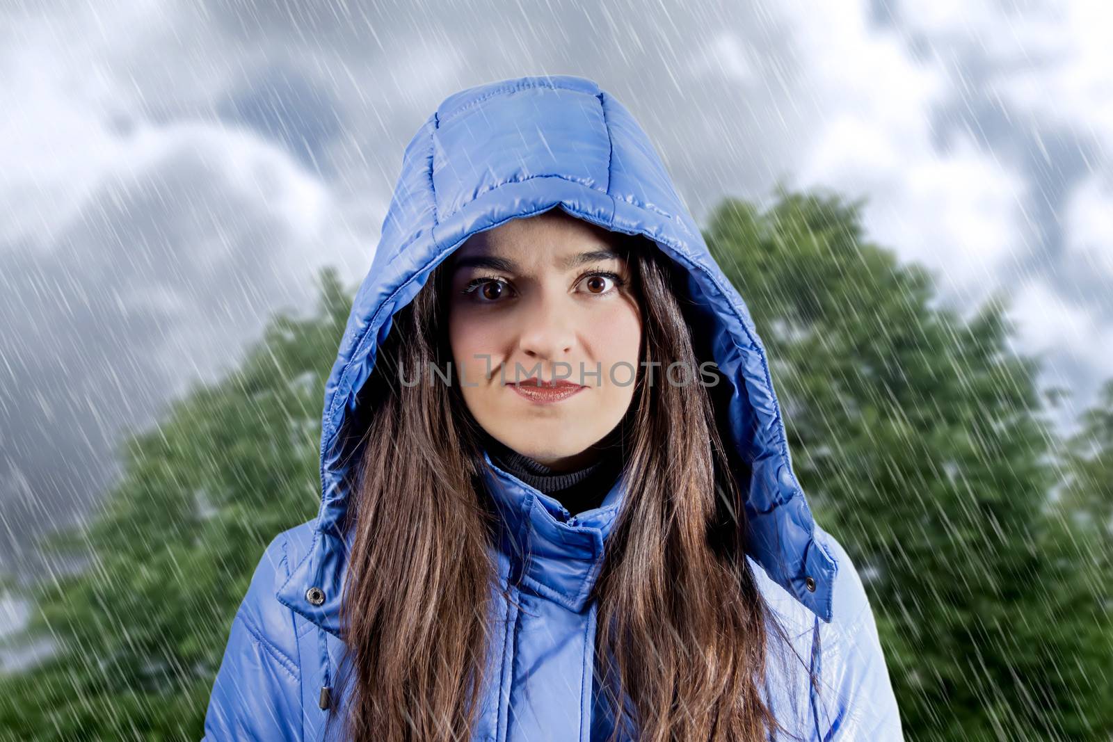 Portrait of serious beautiful young girl wearing a blue raincoat with hood in a rainy day