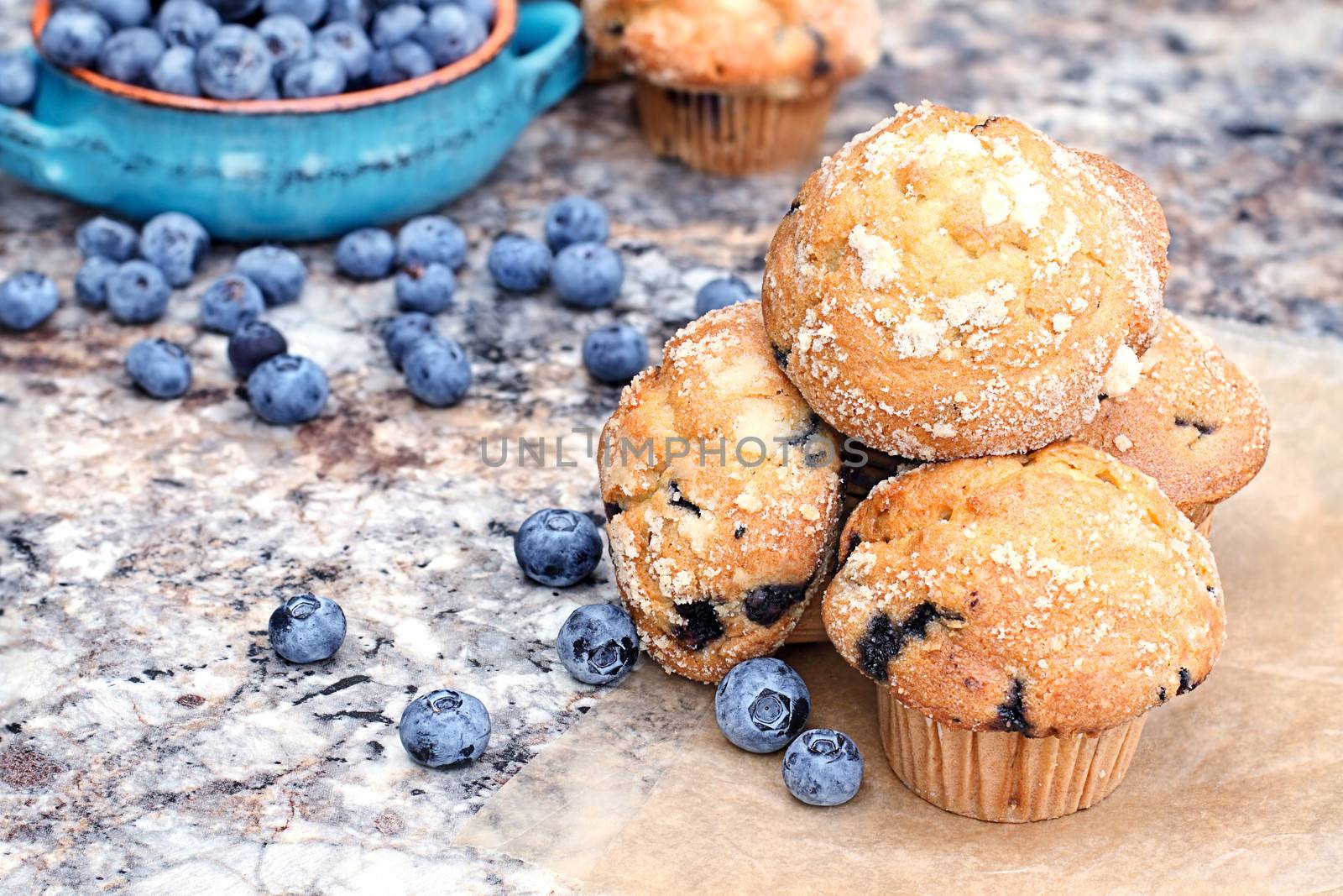 Delicious homemade blueberry muffins with fresh blueberries spilling around them.