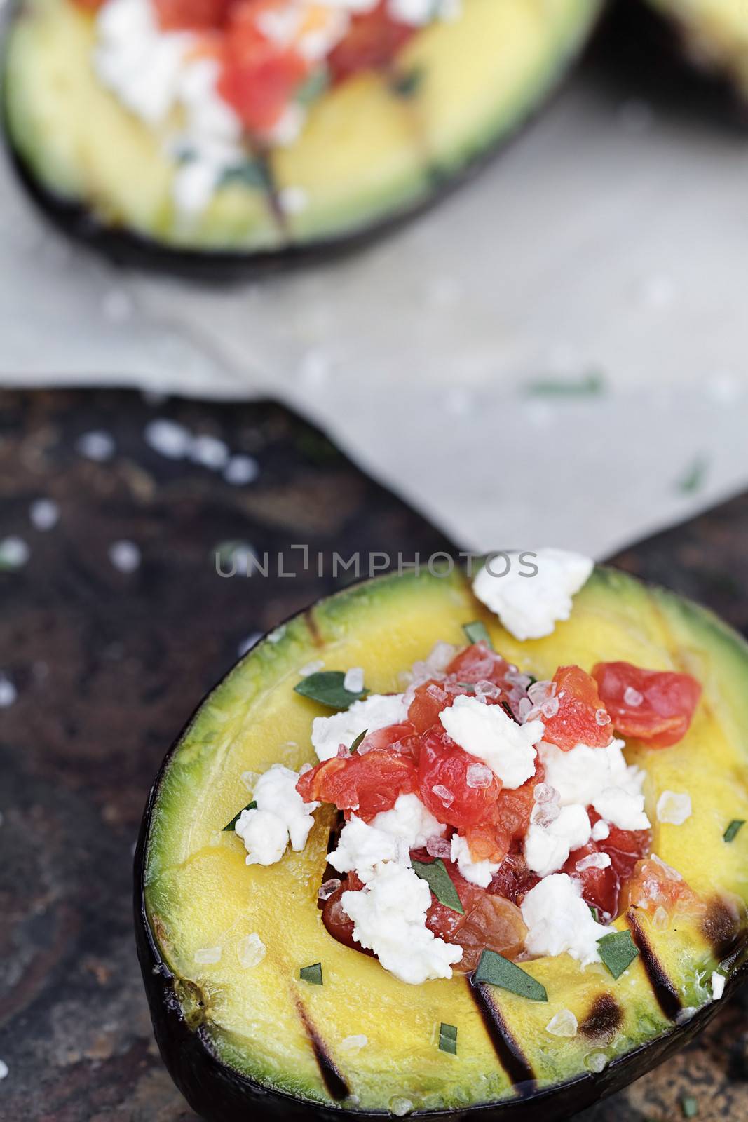 Grilled avocados filled with diced tomatoes and feta cheese and garnished with olive oil and freshly chopped parsley. 