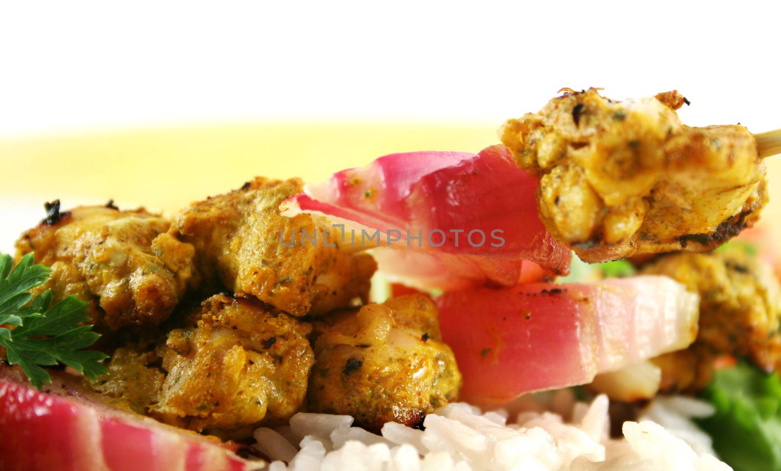 Backlit chicken tandoori skewers with red onion lying on their side and a rocket salad.