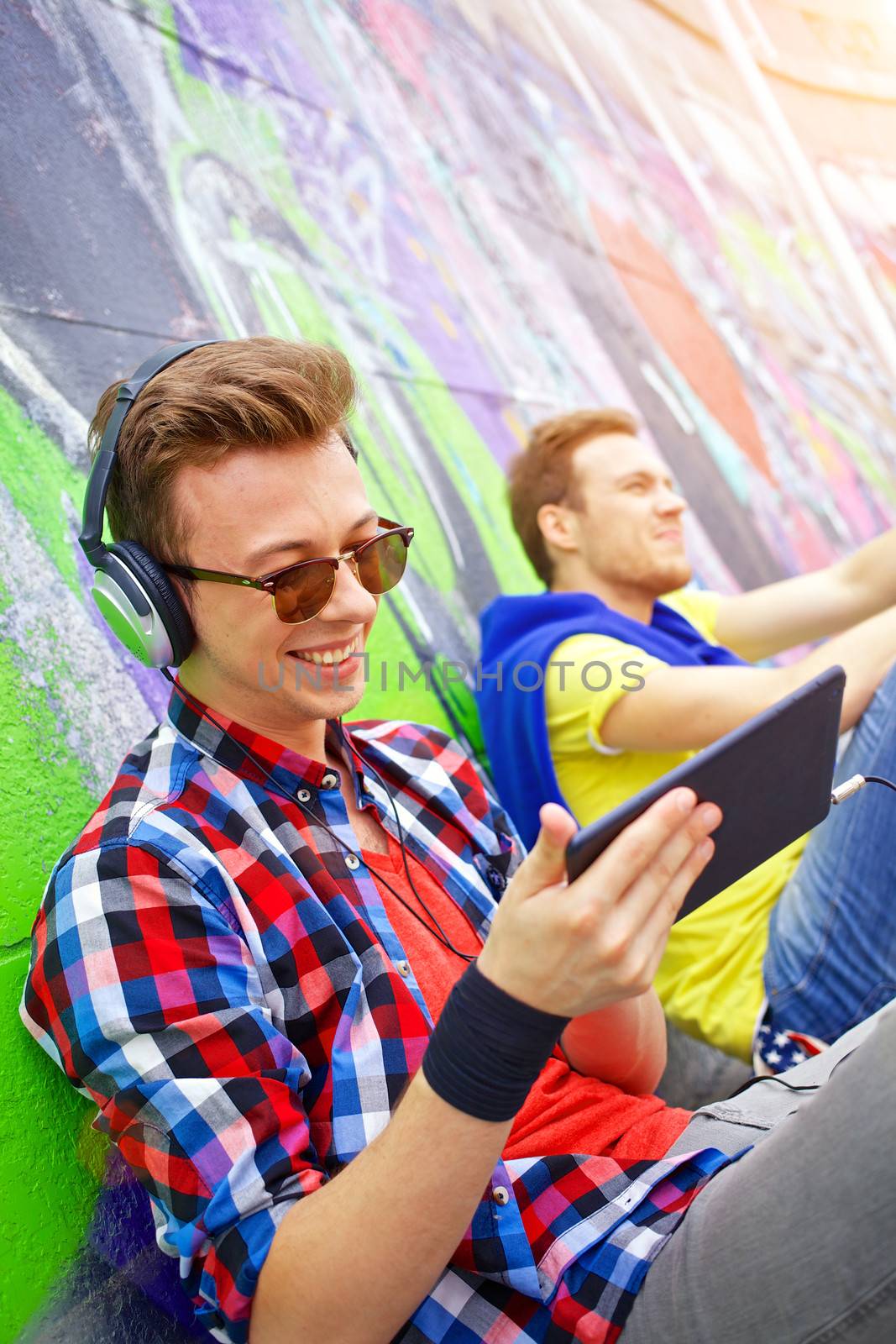 Happy teens boy with his friend by painted wall sunrise listening to music. Vertical view