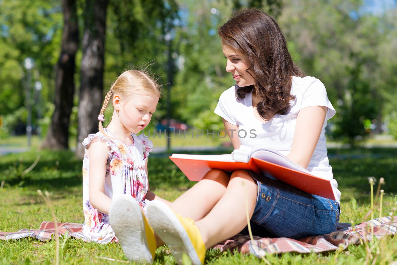 girl with the teacher reading a book together in the summer park
