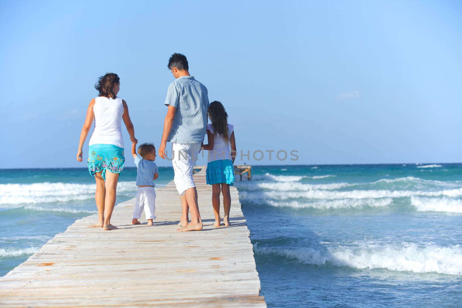 Family of four on wooden jetty by the ocean. Back view