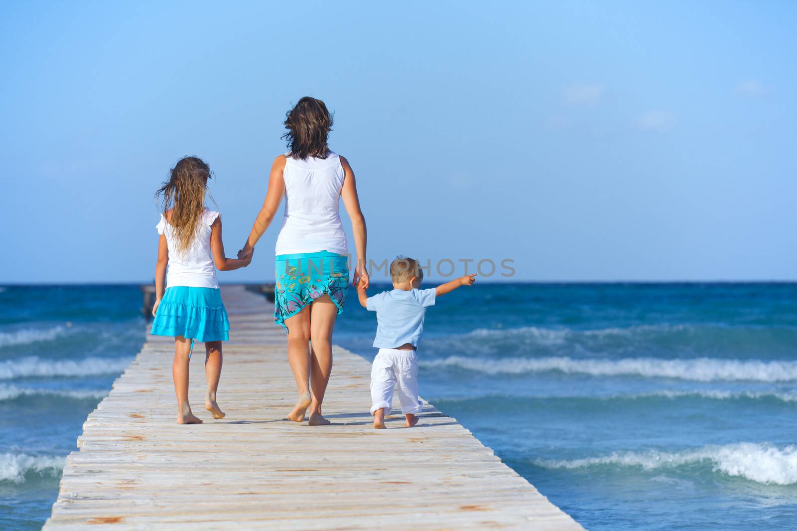 Mother with his two kids walking on wooden jetty by the ocean. Back view