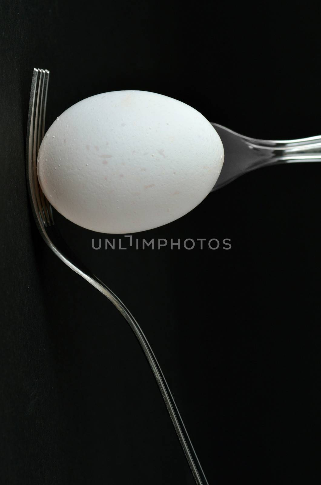 an egg and two forks on black background