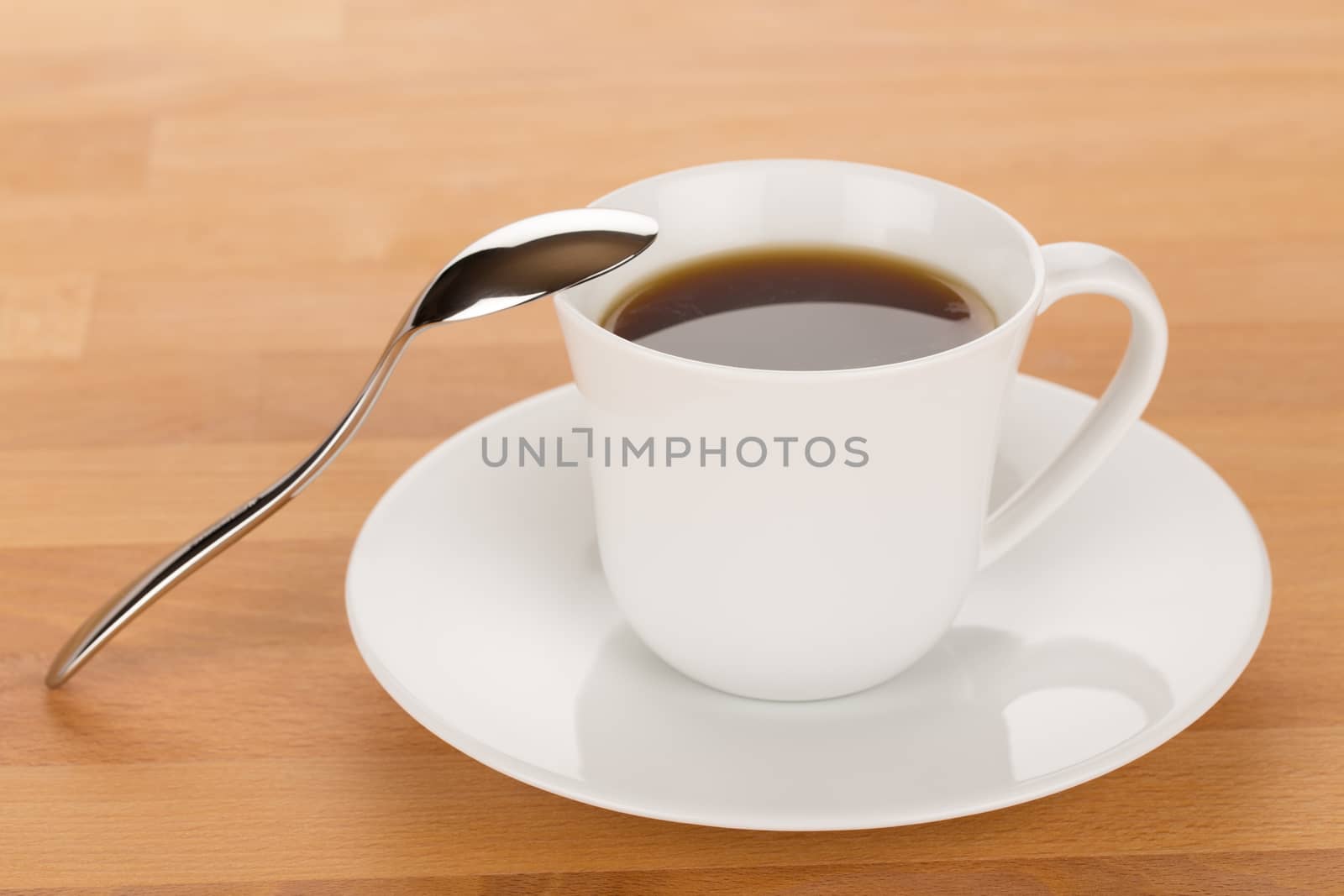Cup of coffee and silver spoon on wooden table close up.