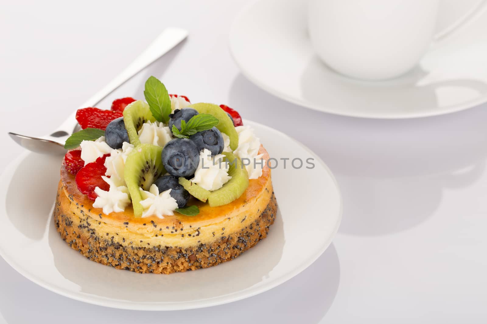 Cheese-cake with strawberry, blueberry, kiwi and cream on white plate.