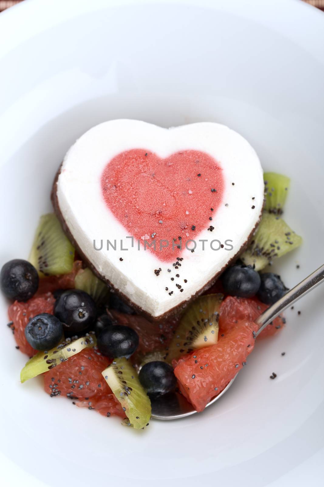 Heart ice cream with blueberry, grapefruit and kiwi on white plate.