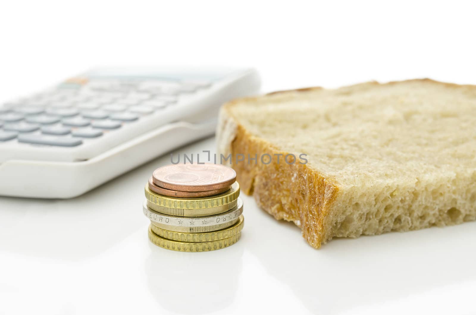 Slice of bred, Euro coins and calculator on a white desk. Concept of saving every cent in order to get through the month.