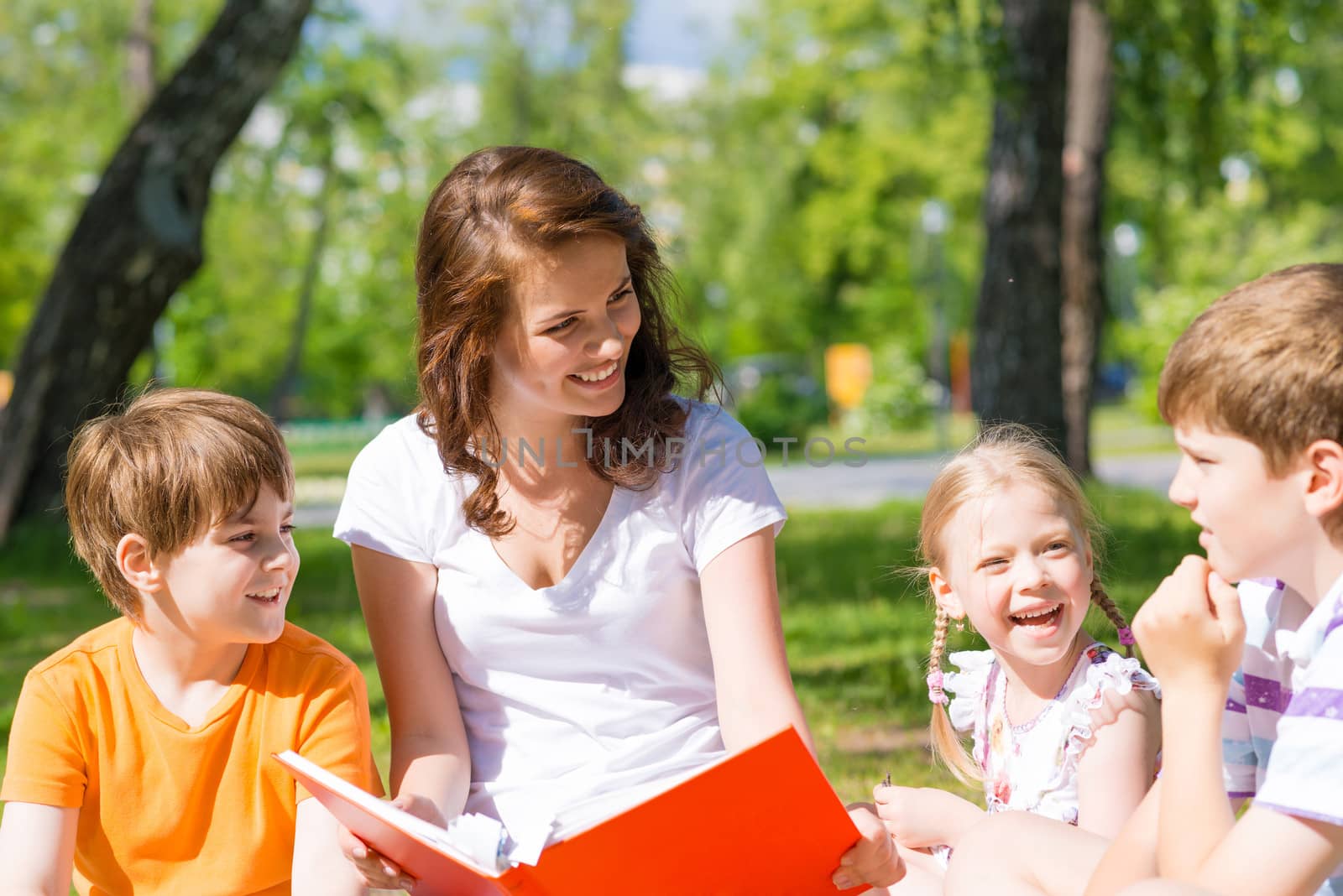 teacher reads a book to children in a summer park by adam121