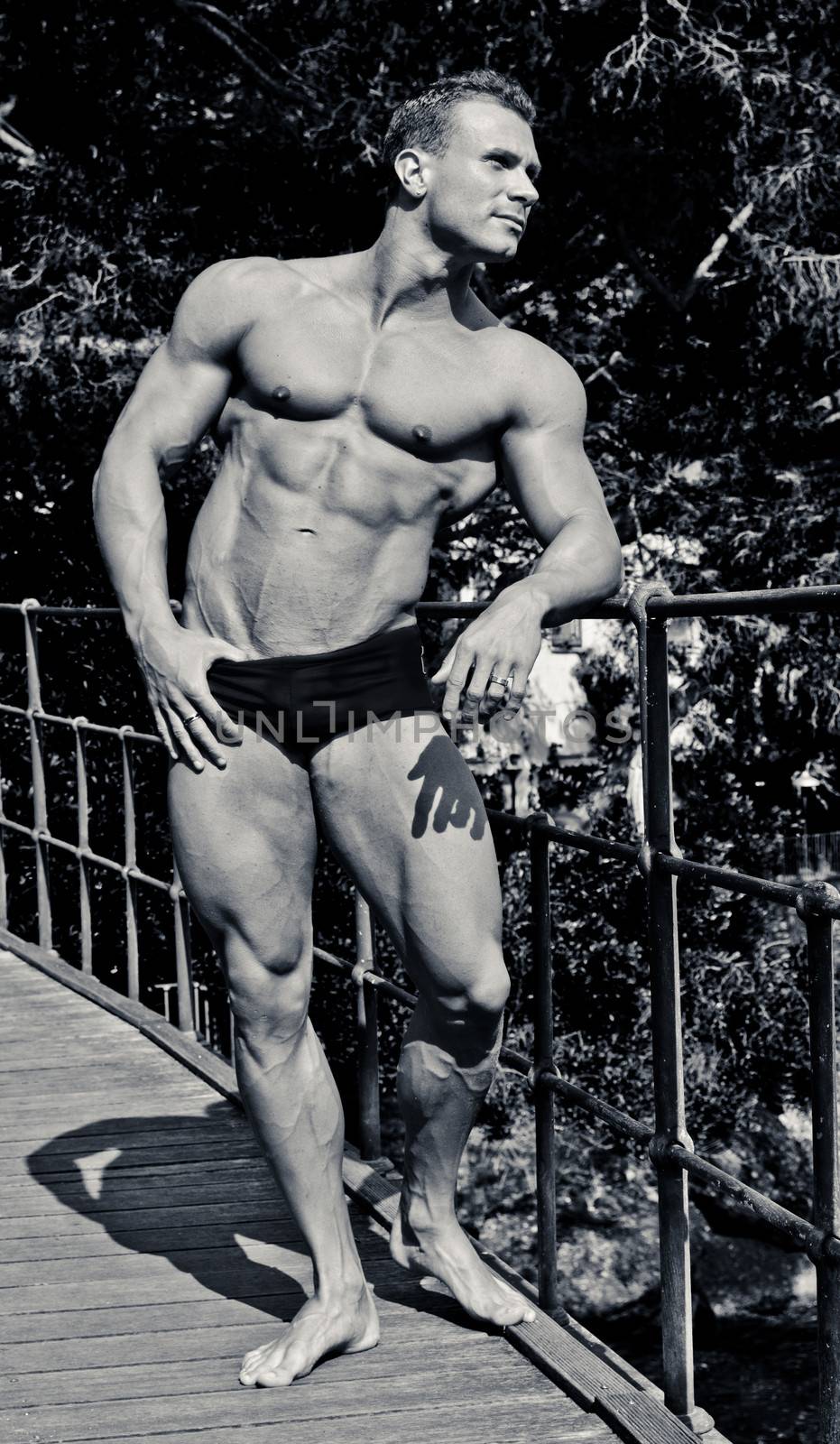 Handsome young muscle man smiling, outdoors, showing muscular body, black and white