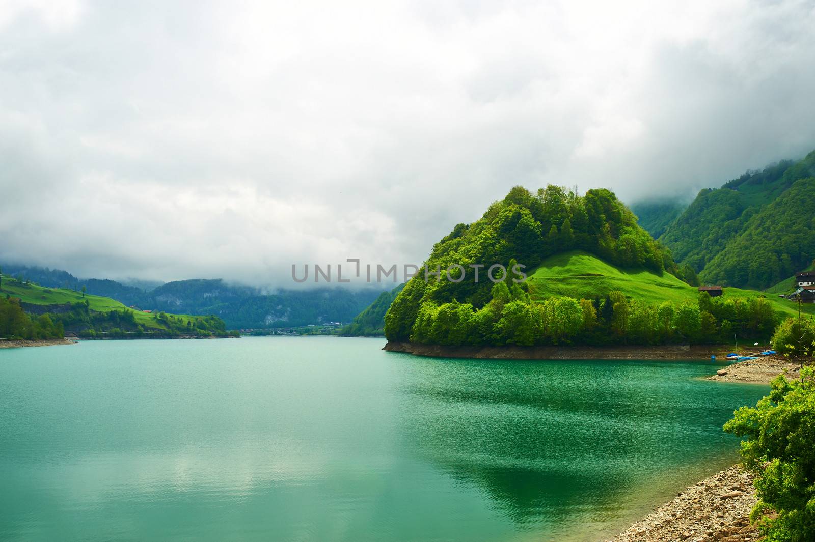 Beautiful emerald mountain lake in Switzerland under low clouds