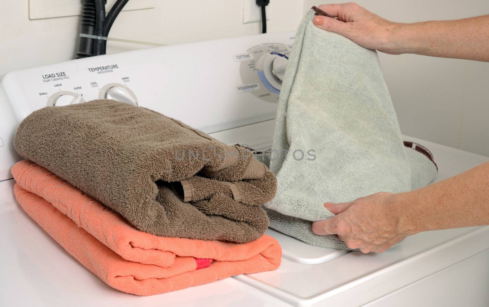 woman doing laundry and folding clean towels near washer and dryer