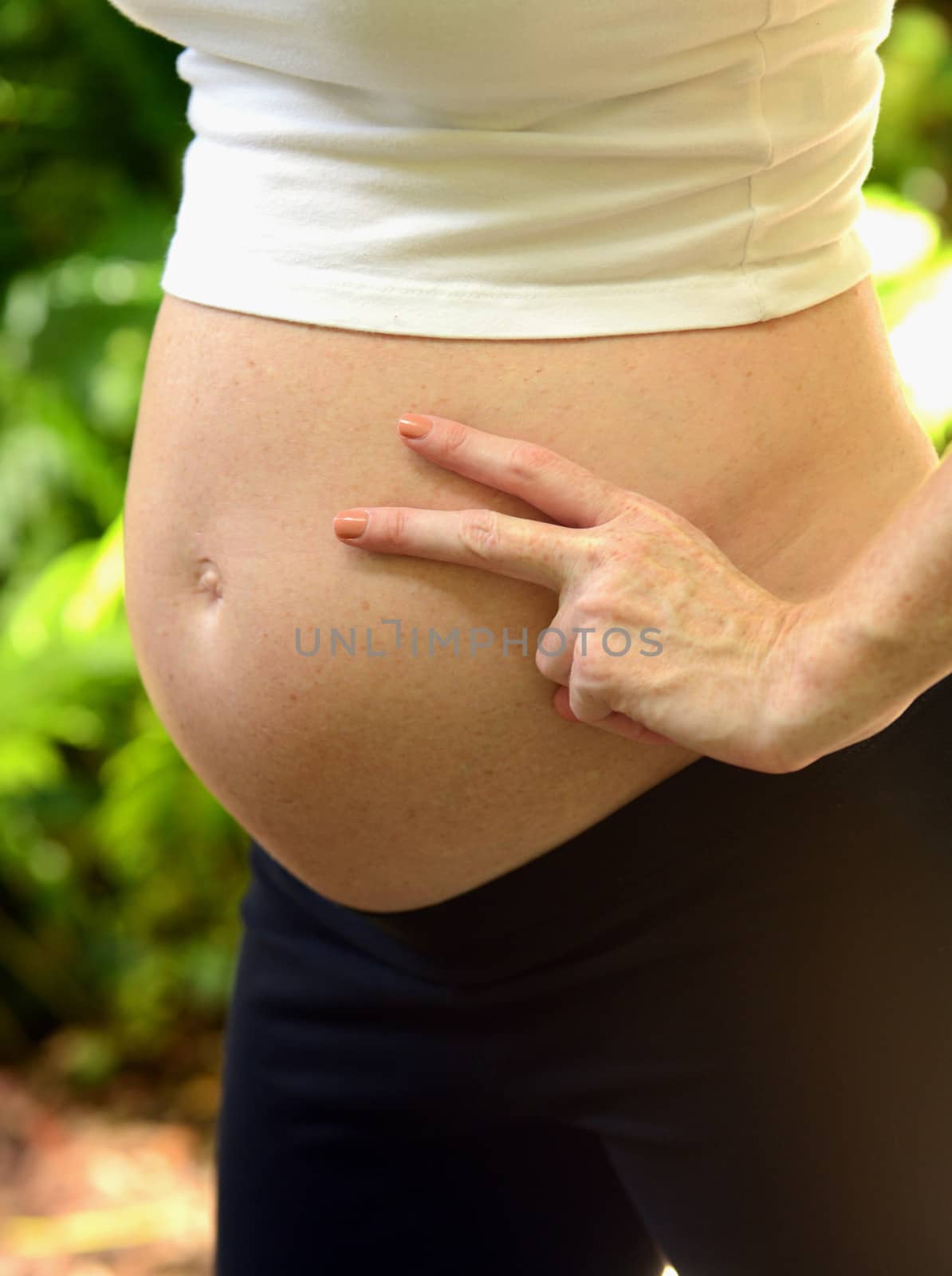 pregant woman holding up a peace sign next to her baby bump