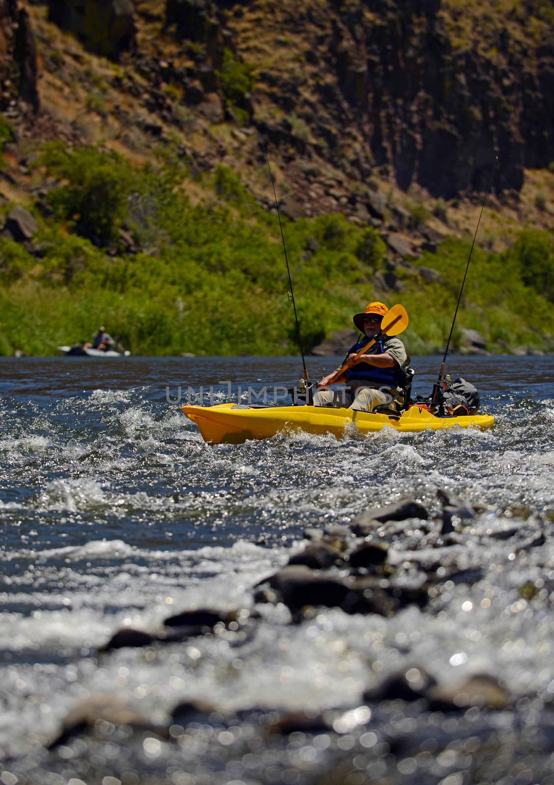 man fishing near rapids in a river in the wilderness while paddling a kayak
