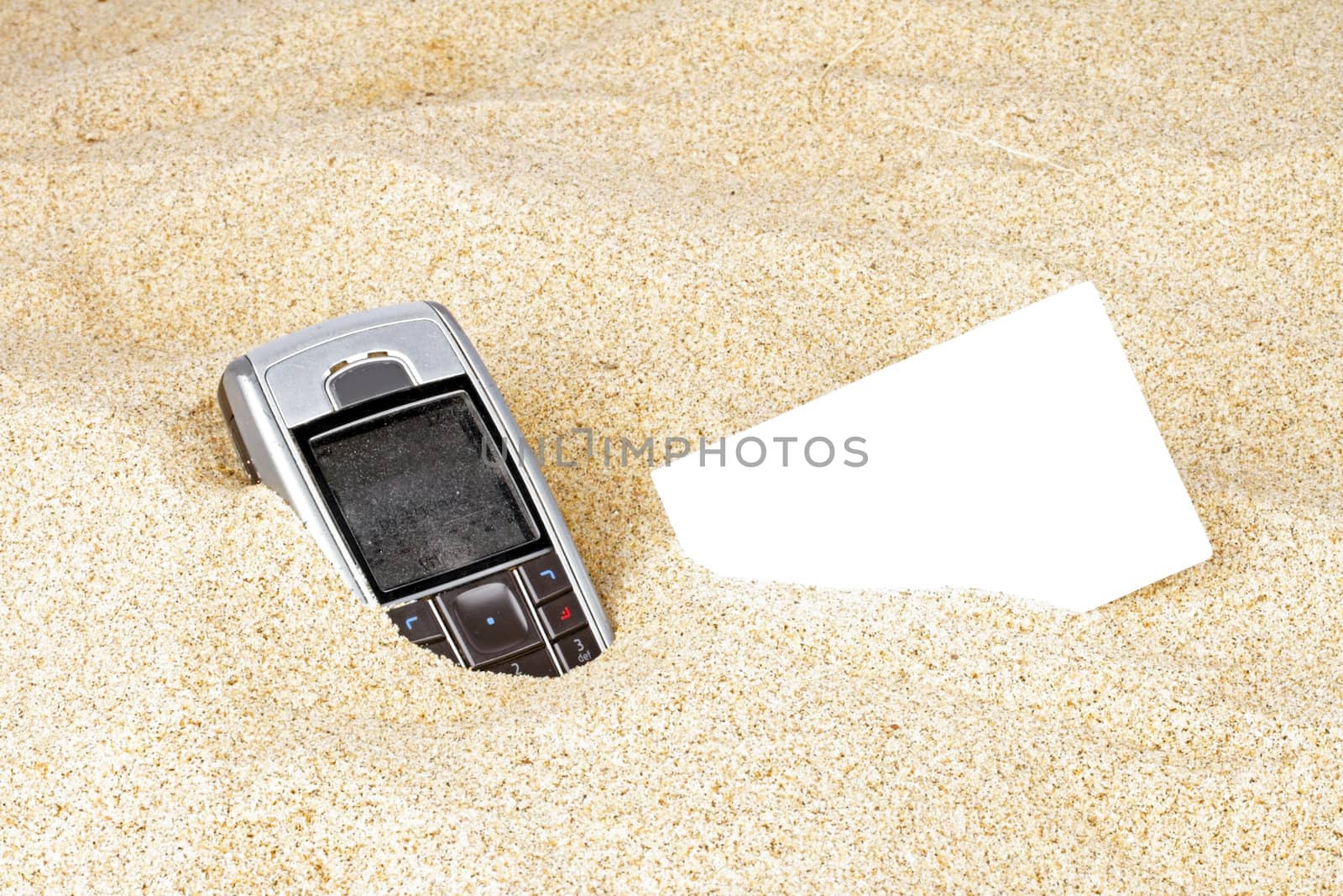 Mobile phone  with business card in the sand