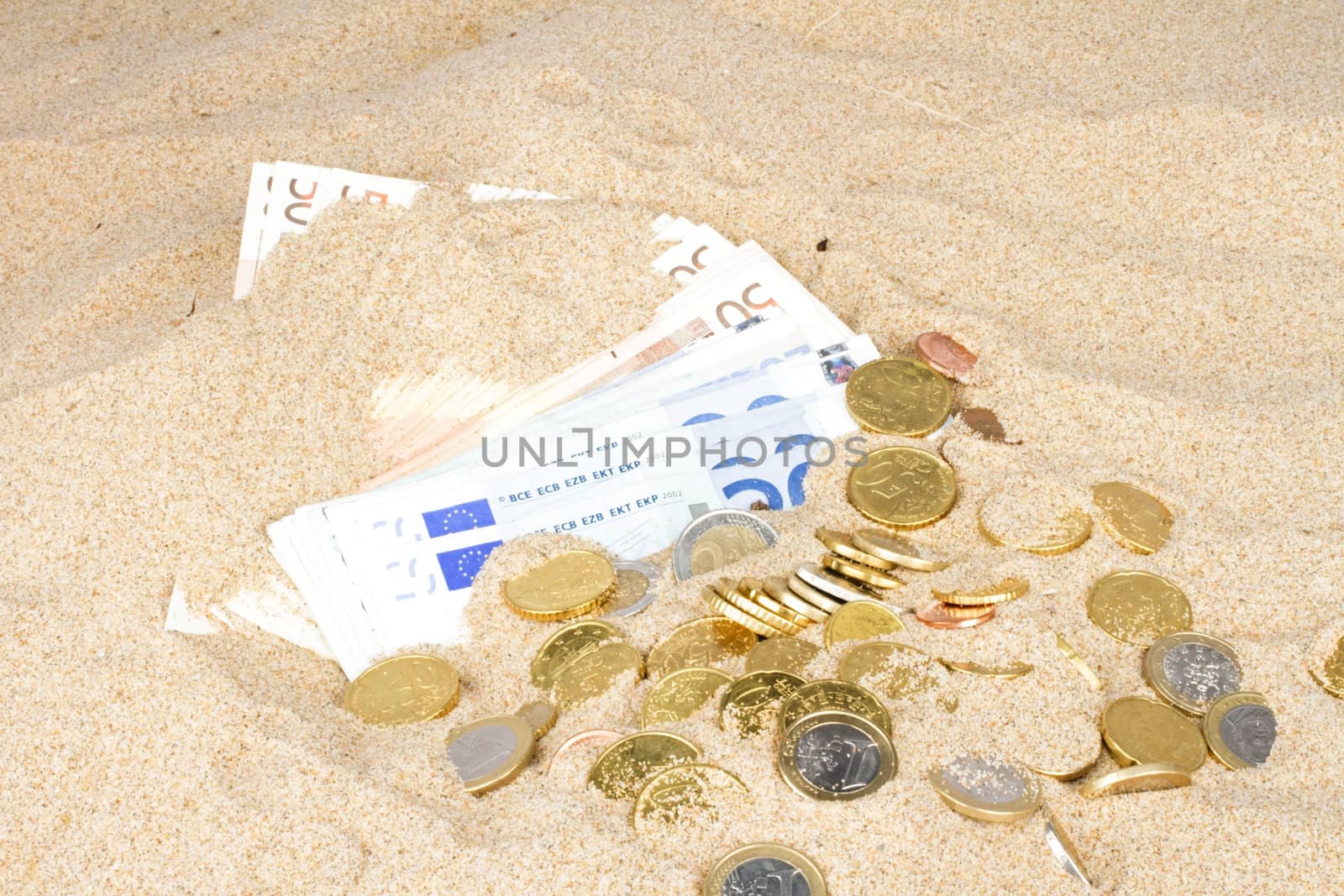 Euro bank notes and coins in the sand