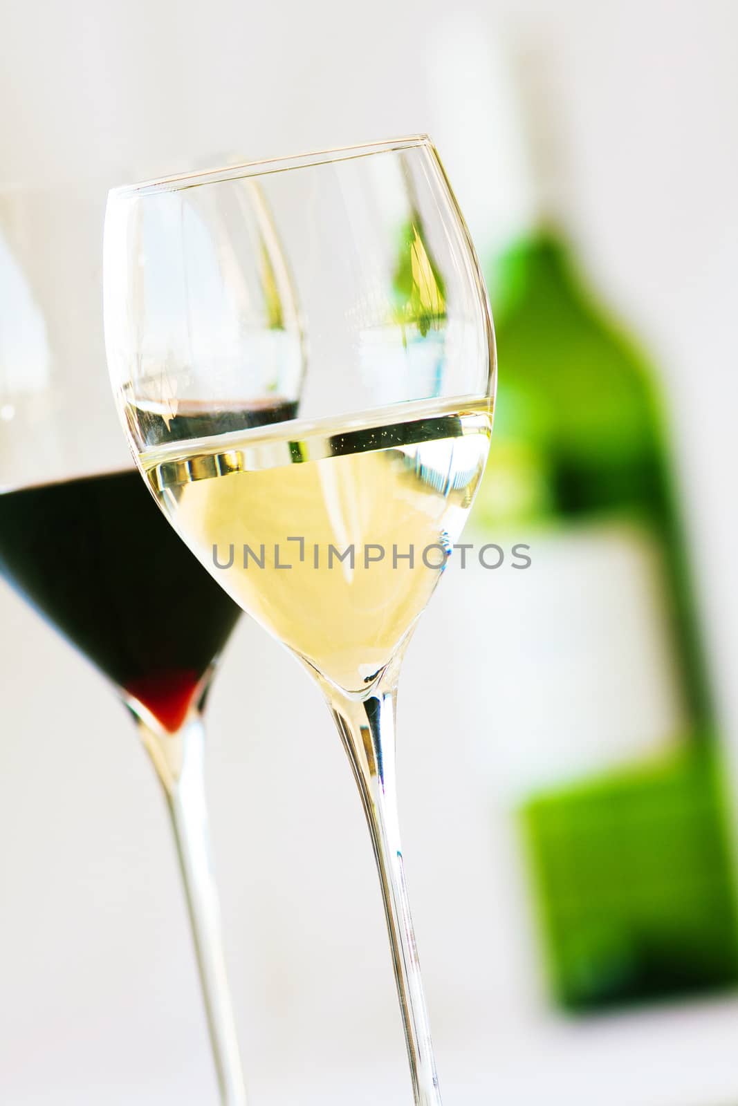 Two glasses of wine, red and white with bottle in the background
