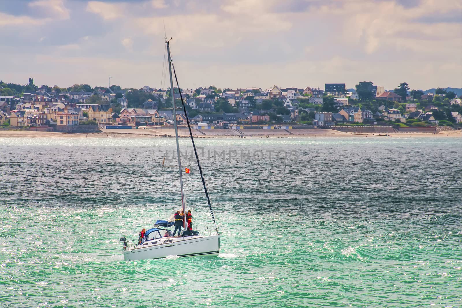 Sailing boat with three people in the sea at the coast with houses