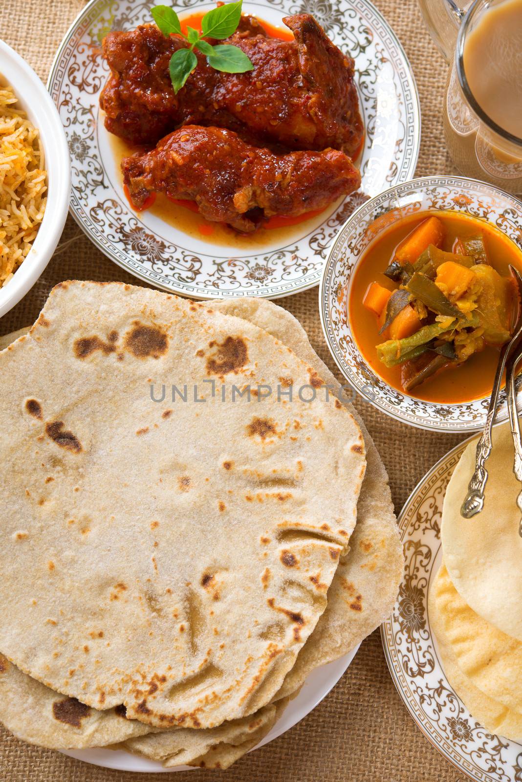 Chapatti roti, curry chicken, biryani rice, salad, masala milk tea and papadom. Indian food on dining table. 