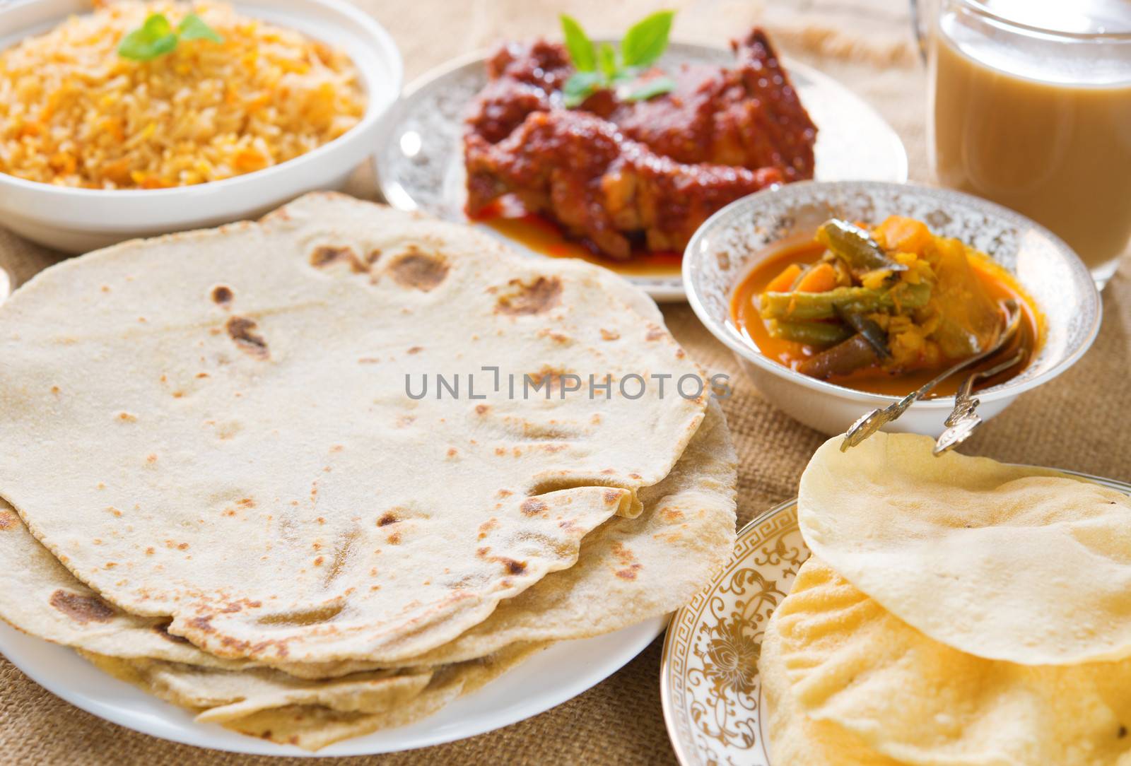 Chapatti roti or Flat bread, curry chicken, biryani rice, salad, masala milk tea and papadom. Indian food on dining table. 