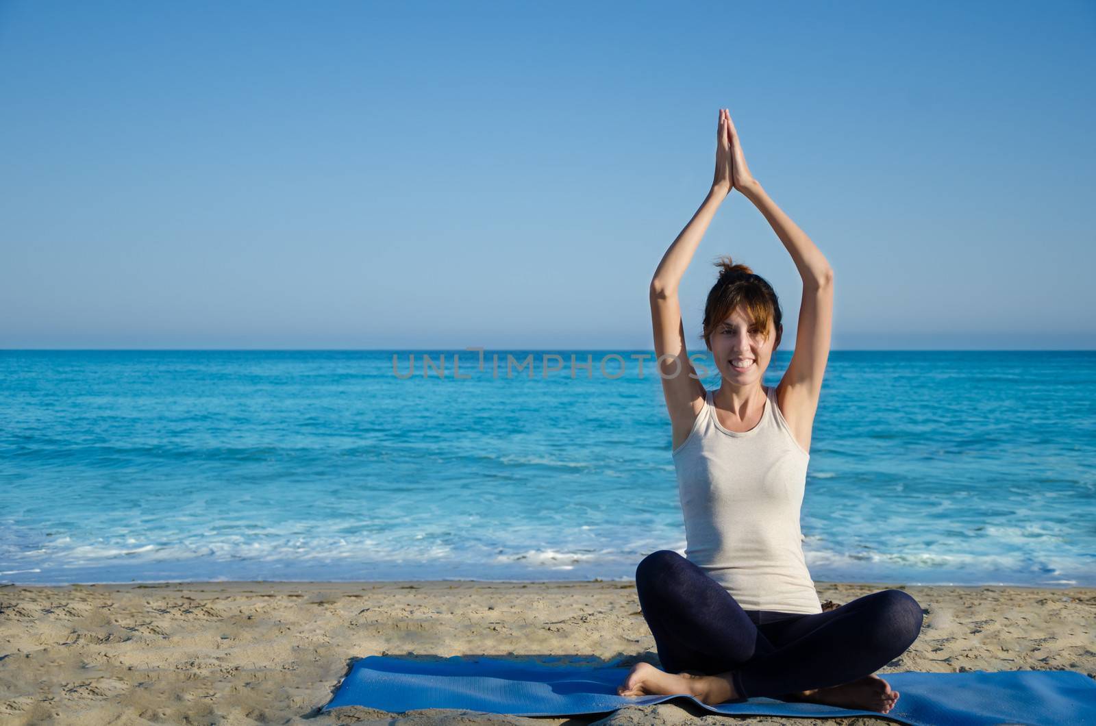 Young pretty woman practicing yoga on the beach by the ocean 