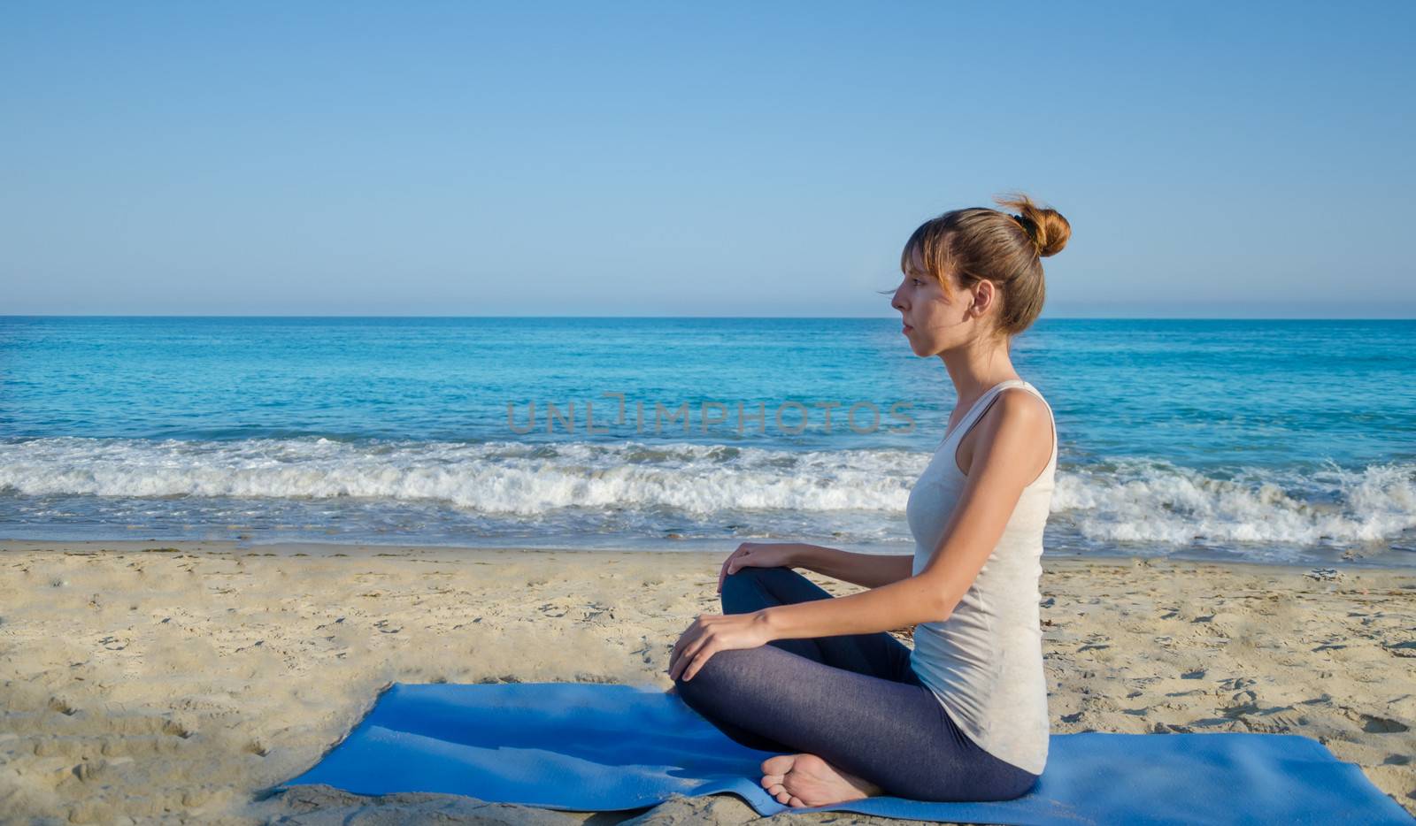 Young pretty woman practicing yoga on the beach by the ocean 