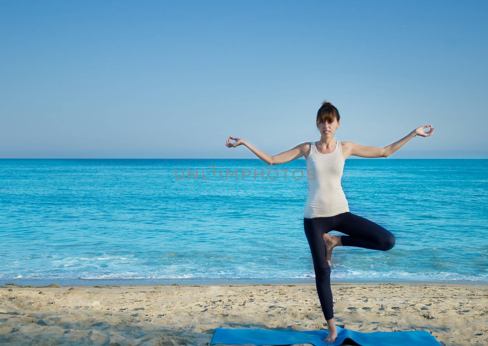 Young pretty woman practicing yoga on the beach by the ocean 