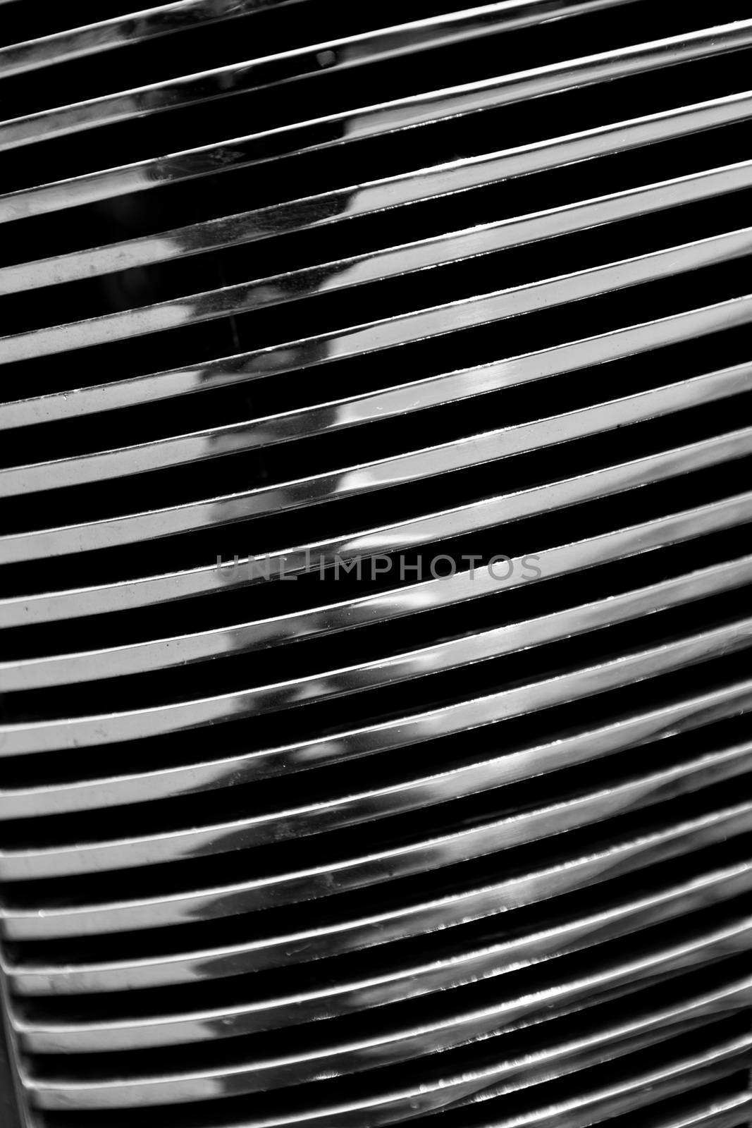 Black and white close up view of a chrome automotive grill on an antique classic car. 