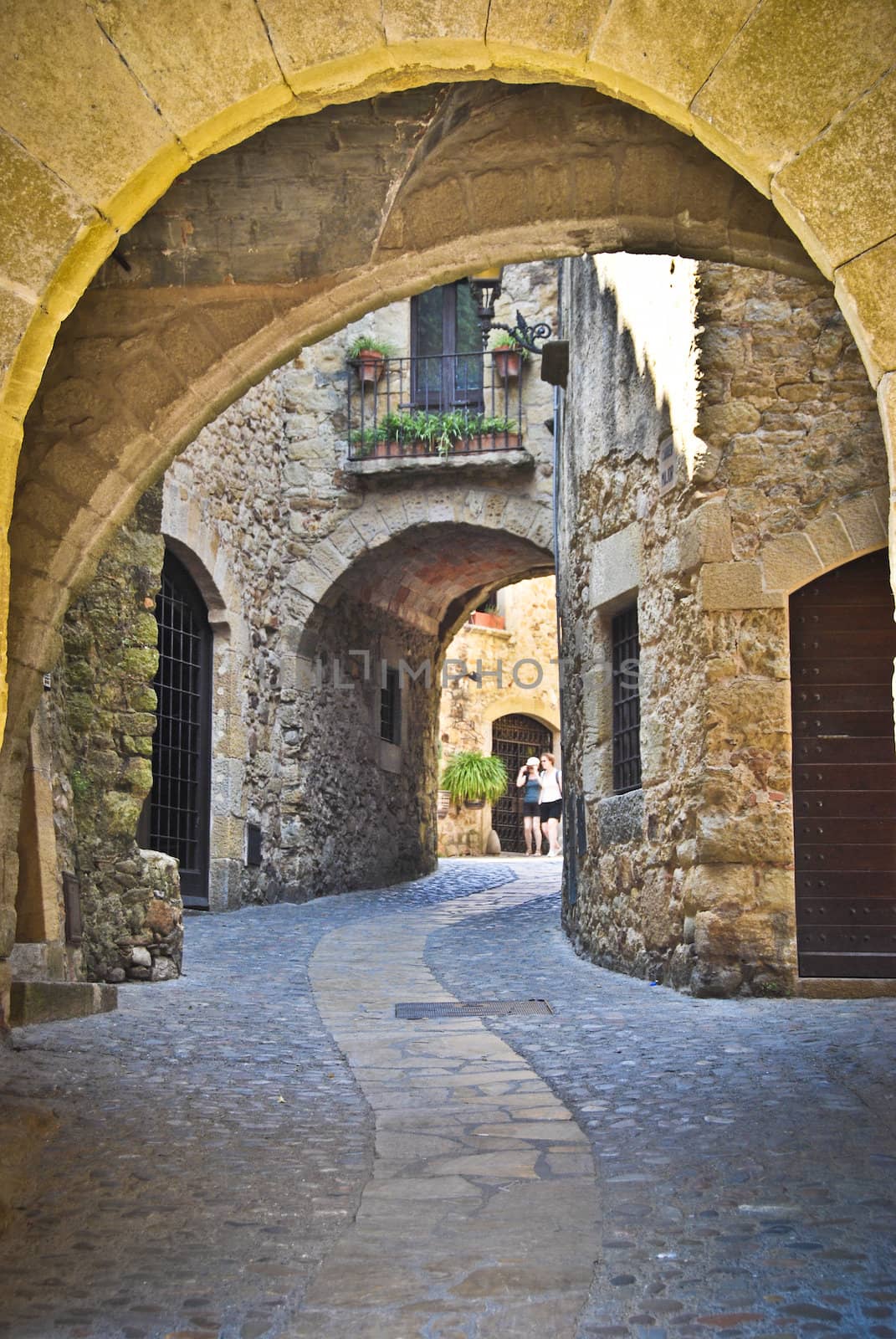 Looking uphill through a medieval arch at a pretty cobbled street in Pals, Spain