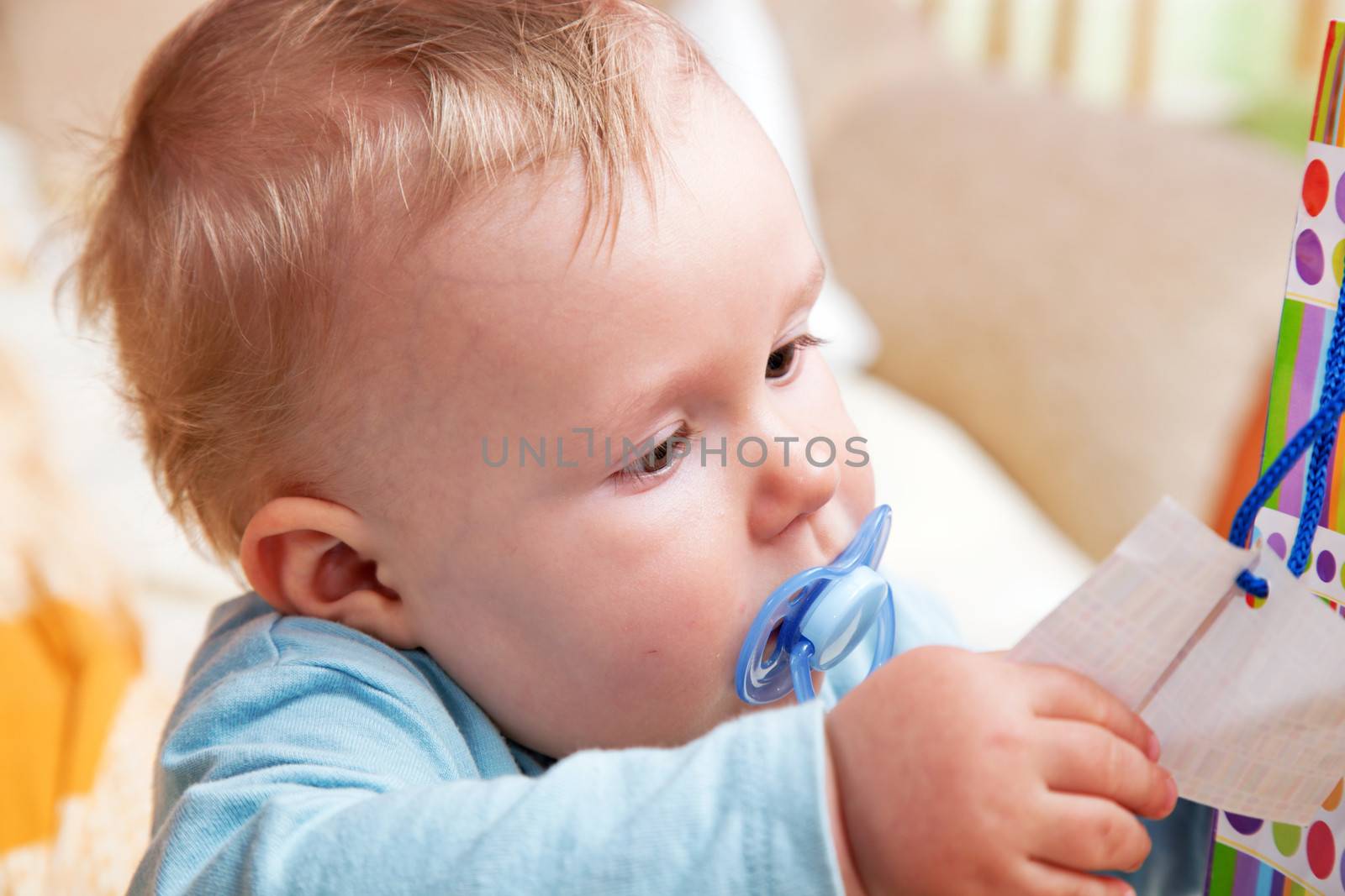 Young baby boy with a dummy in his mouth playing with colorful papers