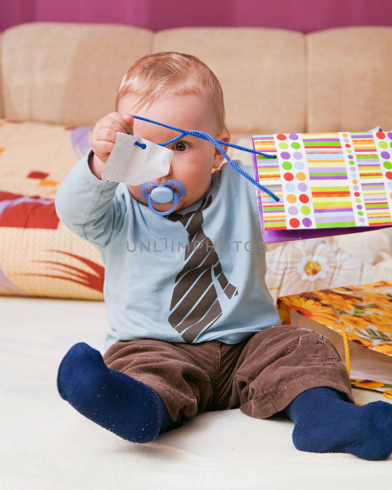 Young baby boy with a dummy in his mouth playing with colorful gift bags