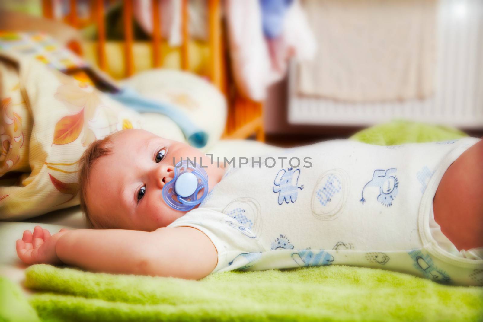 A baby waiting for changing his napkin, lying on bed and looking at the camera