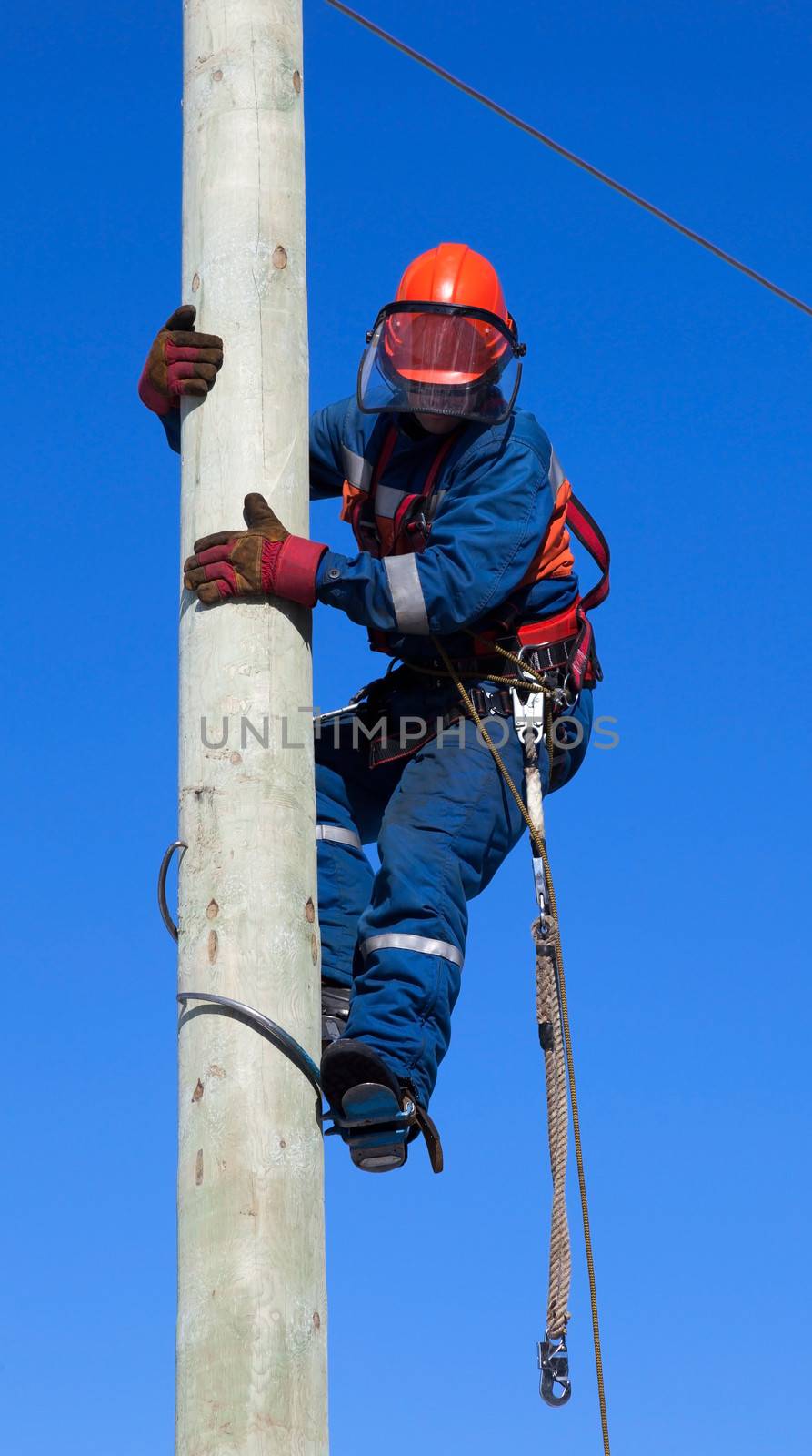 
Electrician climbs the pole power lines against the blue sky
