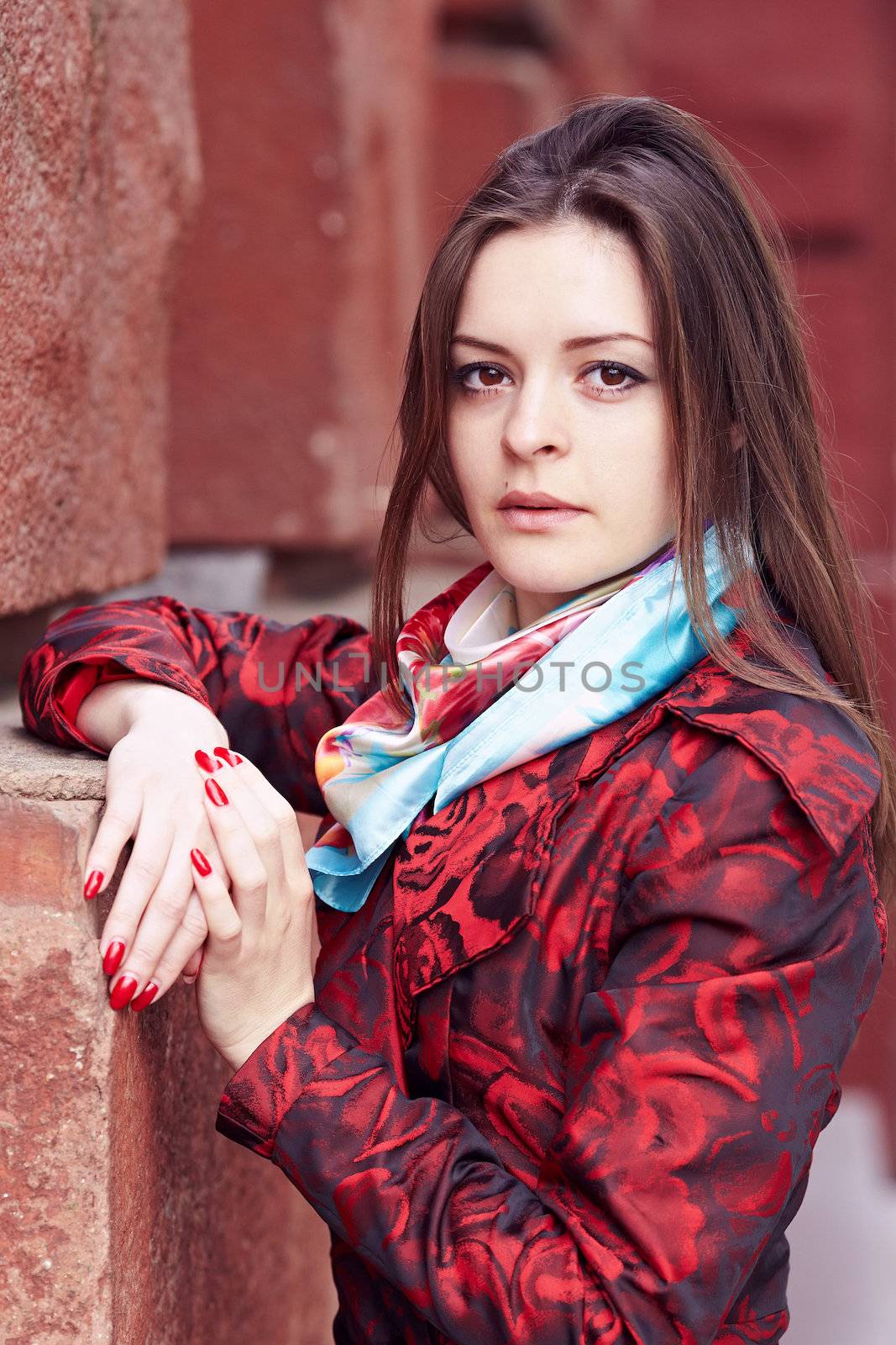 Beautiful girl in a red cloak against a brick wall