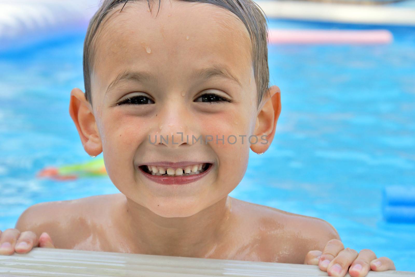 A happy six year old boy enjoys his summertime in the pool.