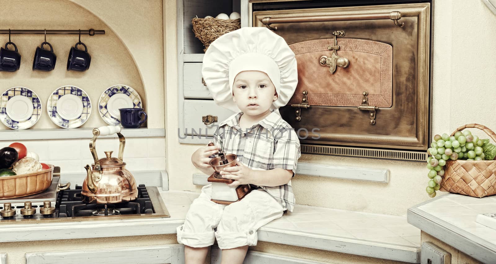 little boy sits on a kitchen table and plays the cook by elena_shchipkova