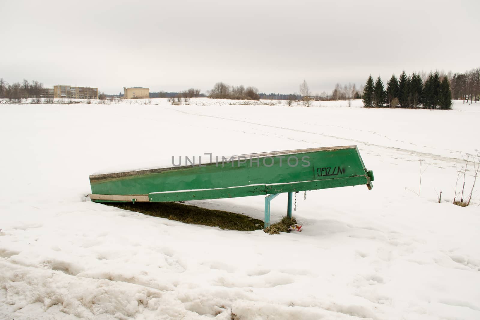 upturned wooden boat covered with snow rest on frozen lake shore bank waiting for warm season in winter.