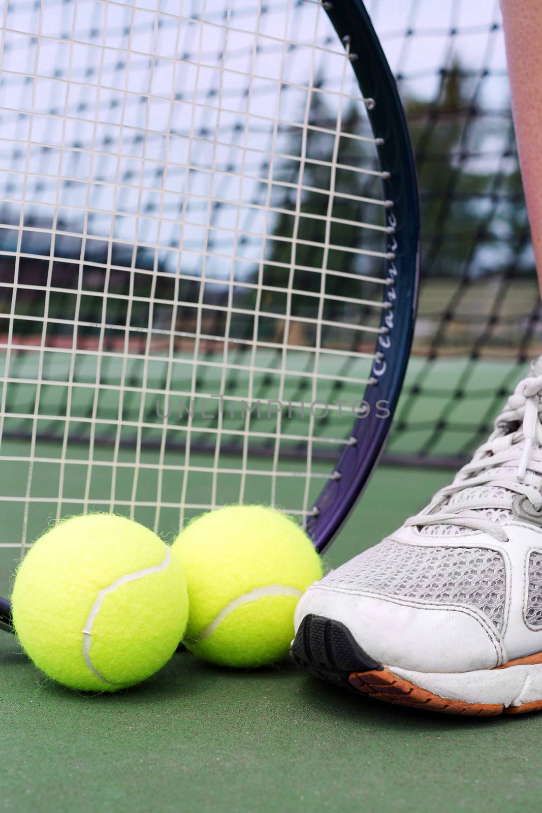 Tennis shoe, racket and balls on a hard court in fron tof net.
