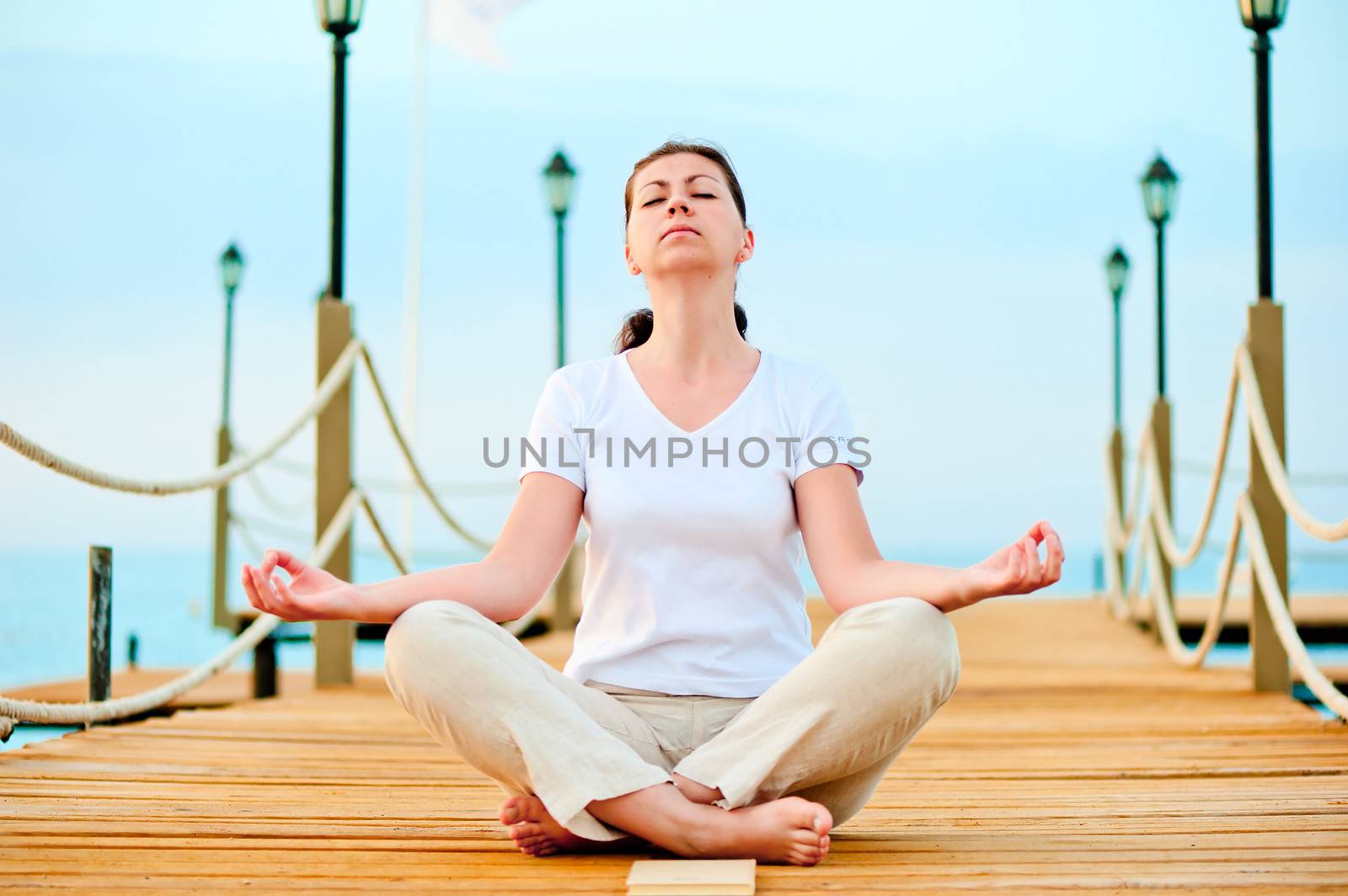 woman dressed in white doing yoga on the pier near the sea