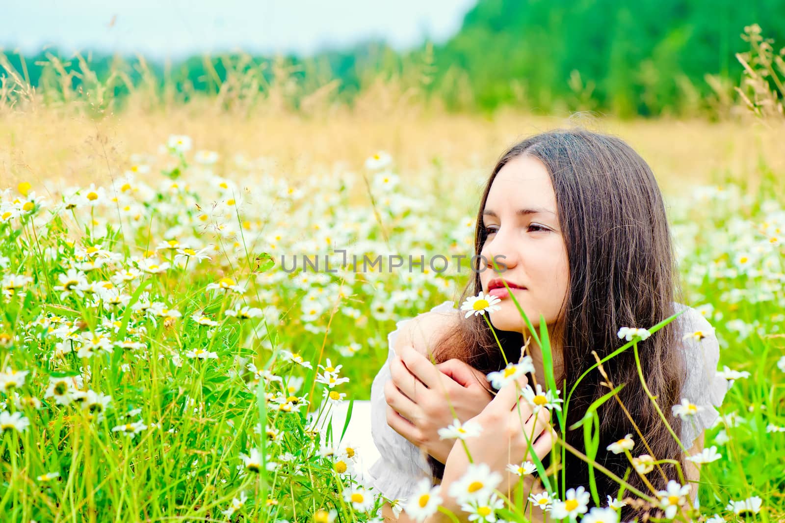 girl resting in a field of chamomile in a white dress