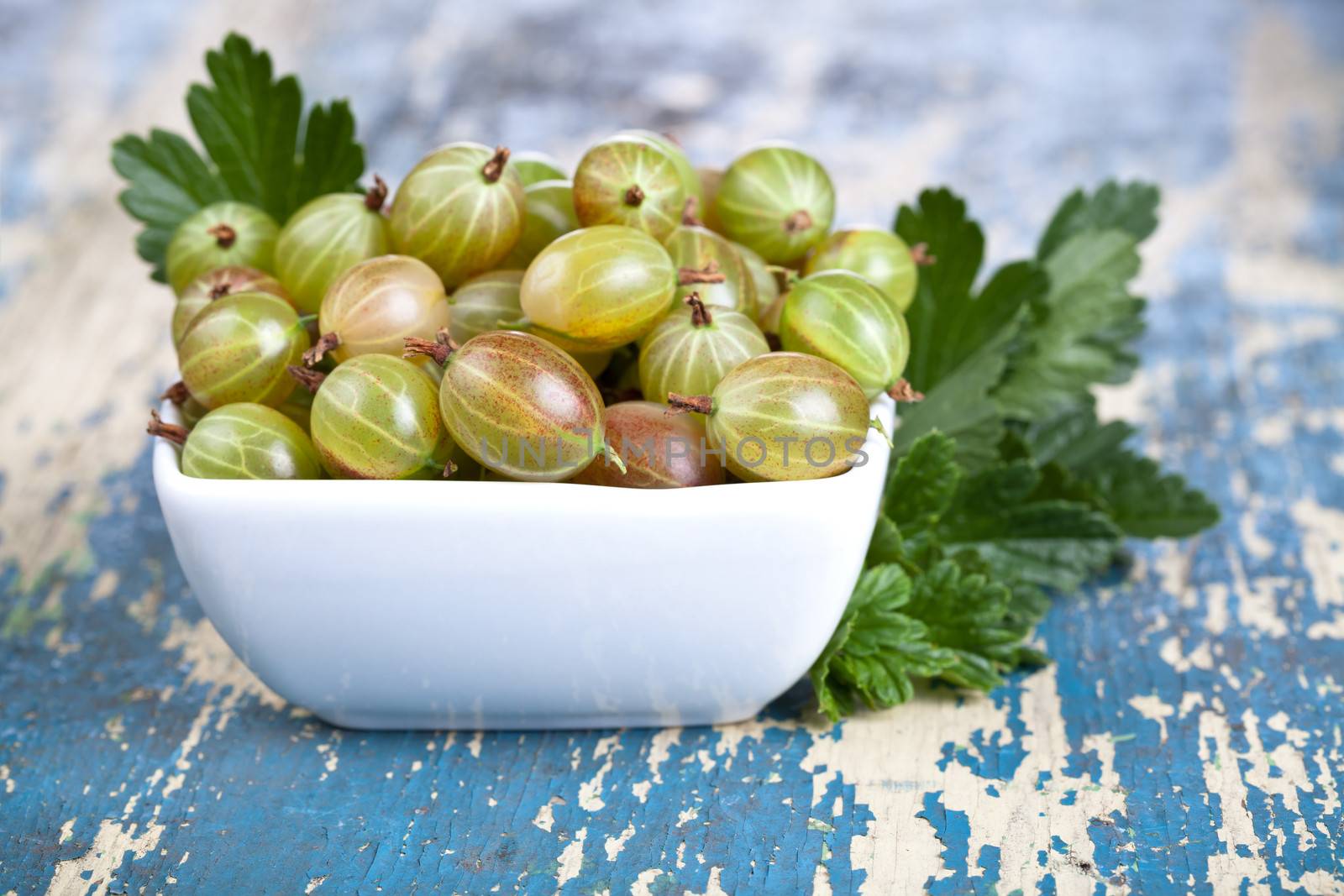 Gooseberries in bowl with leaves on wooden table background