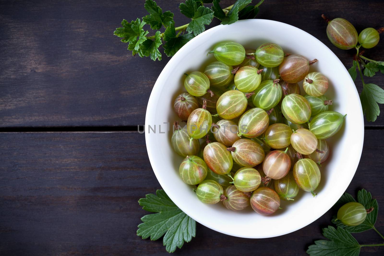 Green gooseberries in bowl on table background with copy space. Top view