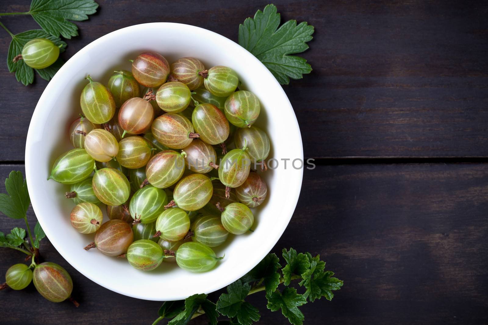 Fresh gooseberries in bowl on wooden background with copy space. Top view