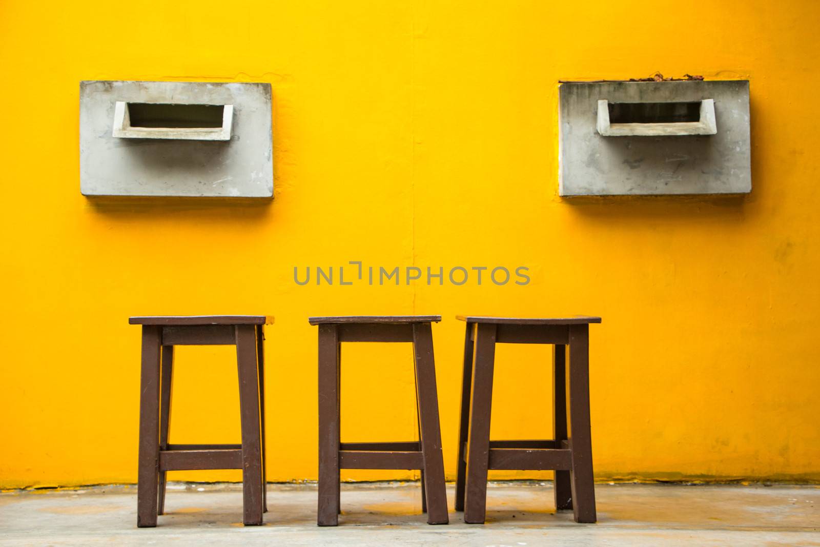 Three chair on concreat stage and yellow wall.