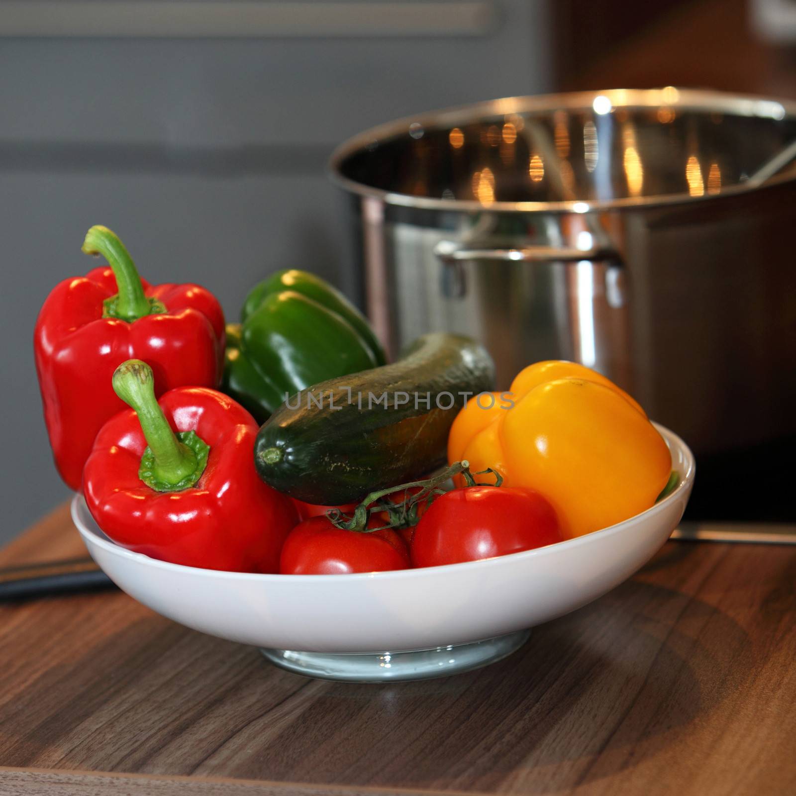 Bowl of colourful fresh vegetables including red, yellow and green bell pepper and ripe red tomatoes standing on a kitchen counter