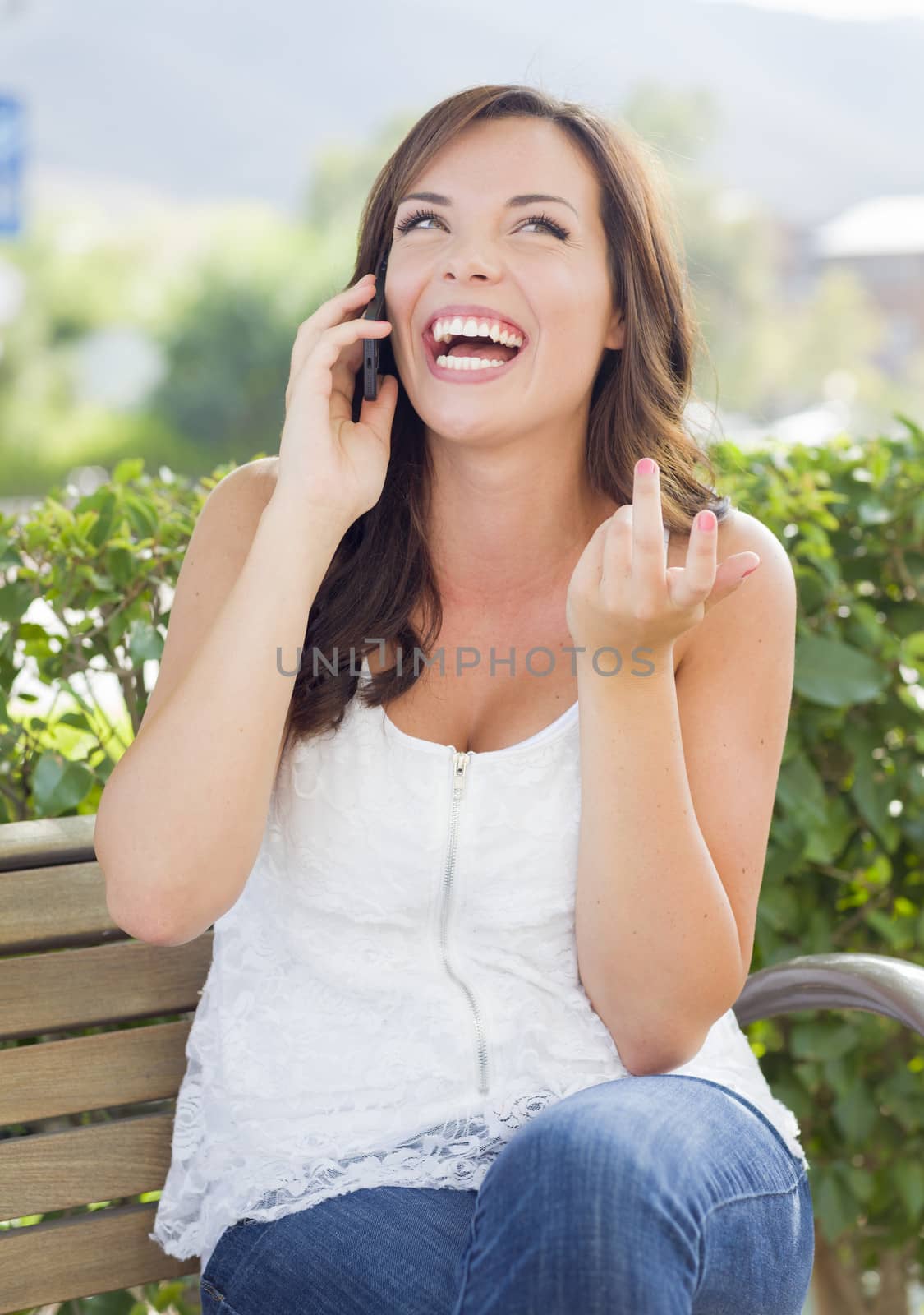 Attractive Young Adult Female Talking on Cell Phone Outdoors on Bench.