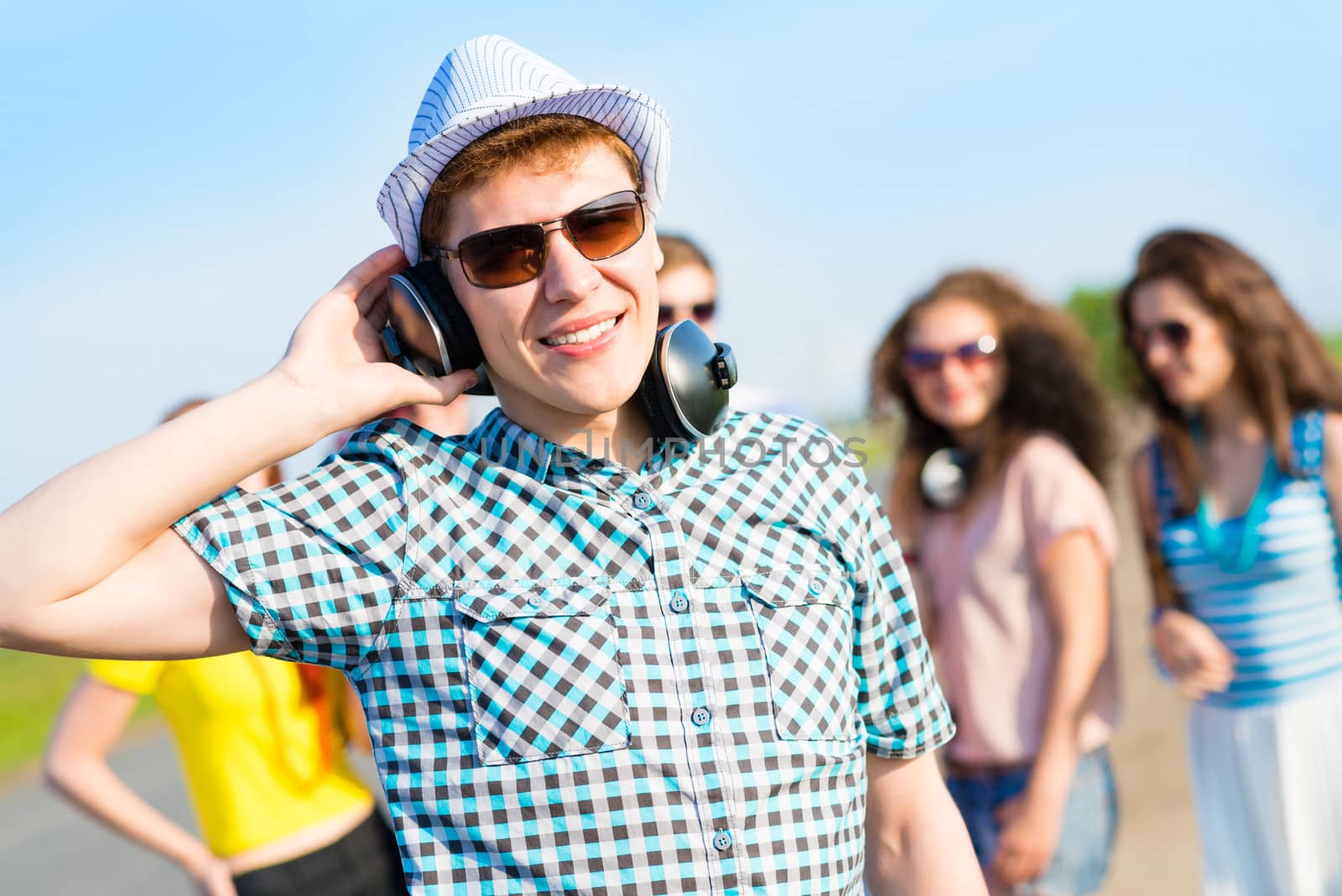 young man in sunglasses, headphones holds a hand on a background of blue sky and friends